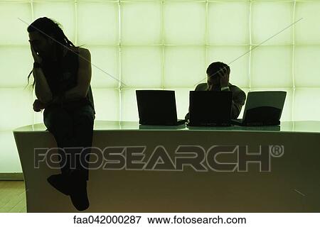 Stock Photo - "Man with dreadlocks sitting on desk, hand under chin, businessman using laptop computer". Fotosearch