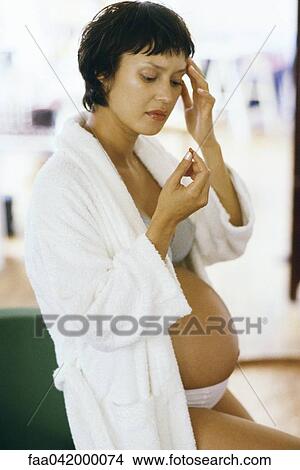"Pregnant woman holding head, looking at pill in hand" View Large Photo Image Picture - "Pregnant woman holding head, looking at pill in hand". Fotosearch