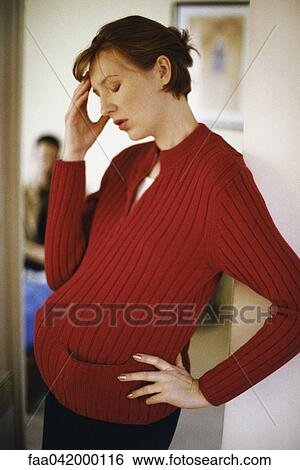 "Pregnant woman holding head, man in background" View Large Photo Image Stock Photograph - "Pregnant woman holding head, man in background". Fotosearch