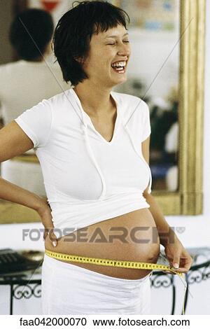 Stock Image - "Pregnant woman measuring stomach with measuring tape, laughing". Fotosearch