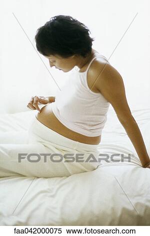 "Pregnant woman sitting on bed, touching stomach, side view" View Large Photo Image Stock Photography - "Pregnant woman sitting on bed, touching stomach, side view". Fotosearch