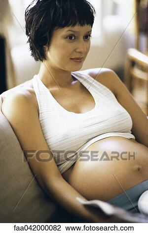 Stock Image - "Pregnant woman sitting on sofa, close-up". Fotosearch