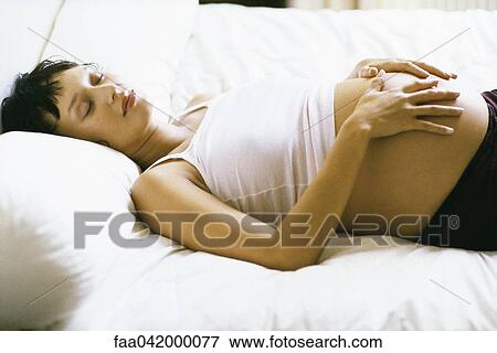 "Pregnant woman sleeping on bed, hands on stomach" View Large Photo Image Stock Photo - "Pregnant woman sleeping on bed, hands on stomach". Fotosearch