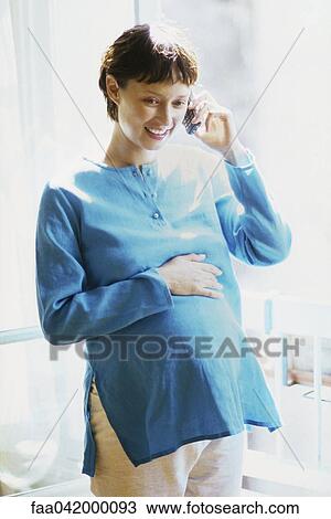 Stock Image - "Pregnant woman talking on cell phone, smiling". Fotosearch
