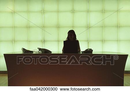 Stock Image - Receptionist at desk smiling at camera. Fotosearch