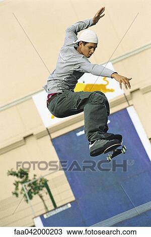 Stock Image - Skateboarder doing midair trick at skatepark. Fotosearch