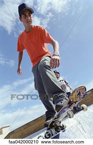Stock Image - Skateboarder perched at edge of ramp preparing to drop off. Fotosearch