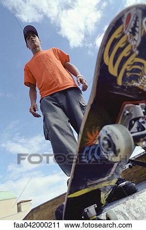 Stock Image - "Skateboarder perched at edge of ramp, low angle view of board". Fotosearch