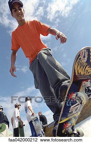 Stock Image - "Skateboarder perched at edge of ramp preparing to drop off, low angle view". Fotosearch