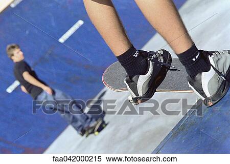 Skateboarder perched at edge of ramp watching friend skate on ramp below View Large Photo Image Stock Photography - Skateboarder perched at edge of ramp watching friend skate on ramp below. Fotosearch