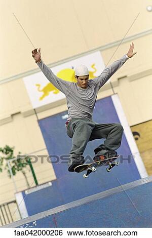 Skateboarder with arms raised doing midair trick at skatepark View Large Photo Image Stock Photograph - Skateboarder with arms raised doing midair trick at skatepark. Fotosearch