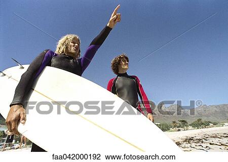 "Surfers on beach, one pointing to distance" View Large Photo Image Stock Image - "Surfers on beach, one pointing to distance". Fotosearch