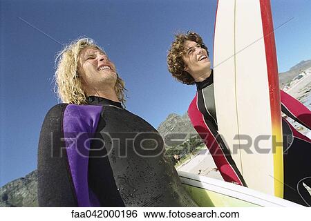 "Surfers on beach, together looking off to distance" View Large Photo Image Stock Photograph - "Surfers on beach, together looking off to distance". Fotosearch