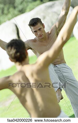 Stock Photograph - "Two martial arts students, face to face with arms raised, in park setting". Fotosearch