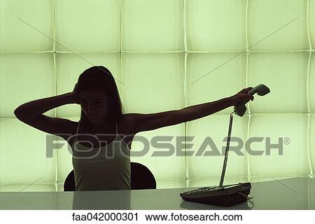 "Woman at desk, holding head, holding phone receiver away" View Large Photo Image Stock Image - "Woman at desk, holding head, holding phone receiver away". Fotosearch