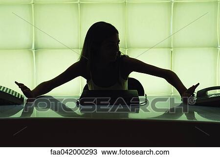 Stock Image - Woman seated at desk reaching for two ringing phones. Fotosearch