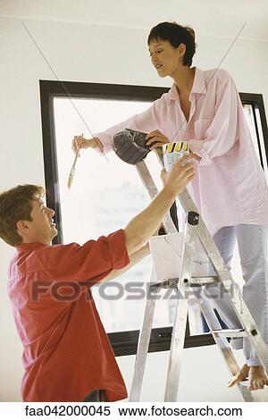 "Woman standing on ladder holding paintbrush, husband holding up paint can" View Large Photo Image Stock Photography - "Woman standing on ladder holding paintbrush, husband holding up paint can". Fotosearch
