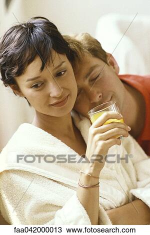 "Woman wearing bathrobe and holding glass of juice, man resting head on her shoulder" View Large Photo Image Stock Image - "Woman wearing bathrobe and holding glass of juice, man resting head on her shoulder". Fotosearch