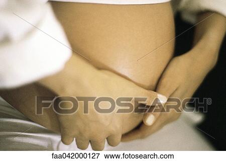 Stock Photo - "Woman's hands on her pregnant belly, close-up". Fotosearch