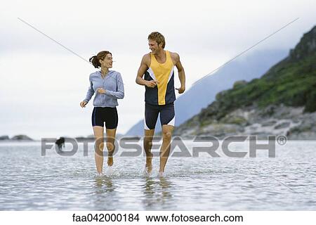 Picture - Young couple running together through shallow water near shore. Fotosearch