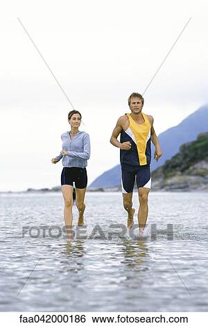Stock Photograph - Young couple running together through shallow water near shore. Fotosearch