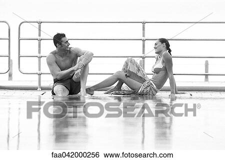 Stock Photograph - Young couple sitting together at poolside smiling at eachother. Fotosearch