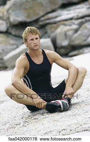 Stock Photo - Young man sitting with soles of feet together doing stretches outdoors. Fotosearch