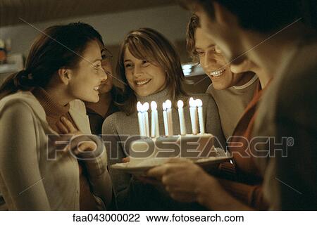 Stock Image - Birthday cake with lit candles being presented to young woman. Fotosearch