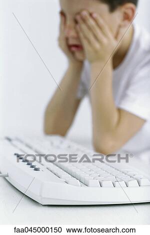 Boy holding head, computer keyboard in foreground View Large Photo Image Stock Image - Boy holding head, computer keyboard in foreground. Fotosearch