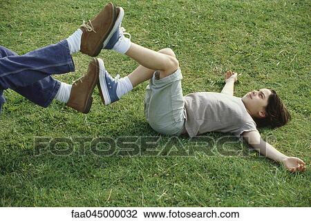 Boy lying on back in grass playing footsies with father View Large Photo Image Stock Image - Boy lying on back in grass playing footsies with father. Fotosearch