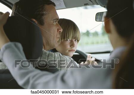 Stock Image - Boy sitting in father's lap in car, looking over shoulder at sister in back seat. Fotosearch