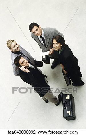 Stock Image - Business associates standing together looking up at camera, high angle view. Fotosearch