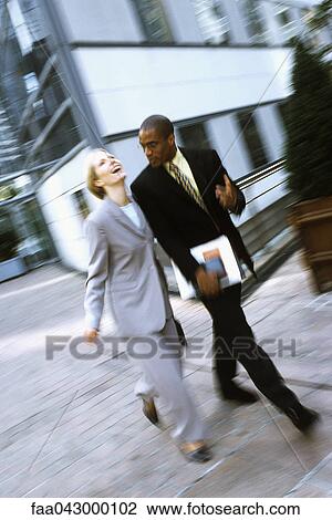 Stock Image - Businessman and businesswoman walking together in conversation, woman laughing. Fotosearch