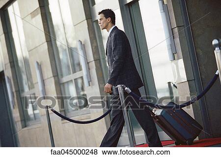 Businessman leaving hotel, pulling suitcase behind him View Large Photo Image Stock Photo - Businessman leaving hotel, pulling suitcase behind him. Fotosearch