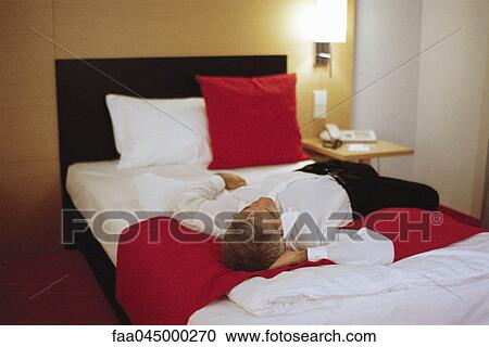 Stock Image - Businessman lying fully clothed on hotel bed. Fotosearch