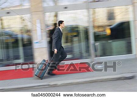 Picture - Businessman running down sidewalk, pulling suitcase behind him. Fotosearch