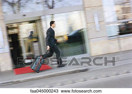 Stock Image - Businessman running down sidewalk, pulling suitcase behind him. Fotosearch