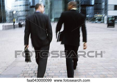 Stock Photo - Businessmen walking together along city sidewalk. Fotosearch