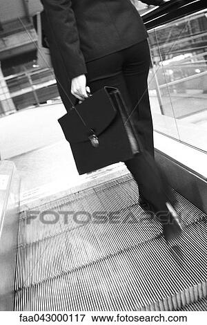 Stock Photo - Businesswoman ascending escalator, rear view. Fotosearch