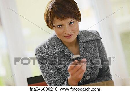 Businesswoman holding cell phone, smiling at camera View Large Photo Image Stock Photograph - Businesswoman holding cell phone, smiling at camera. Fotosearch