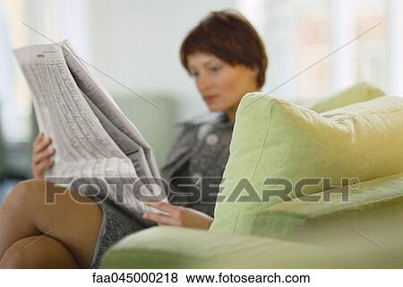 Stock Photo - Businesswoman sitting on sofa reading newspaper. Fotosearch