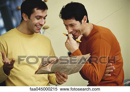 Stock Photography - Casually dressed colleagues looking at newspaper together, smiling. Fotosearch