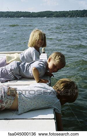 Stock Photograph - Children lying on stomach on pier looking at water. Fotosearch