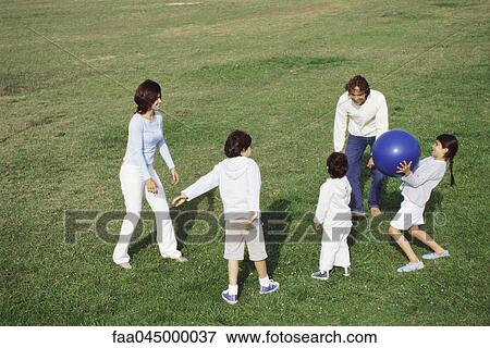 Stock Photo - Family playing with ball in grassy field. Fotosearch