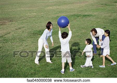 Stock Photo - Family playing with ball in grassy field. Fotosearch