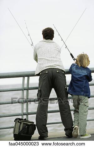 Stock Image - Father and son fishing from pier, rear view. Fotosearch