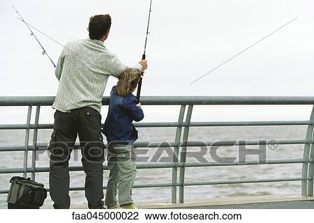 Stock Image - Father and son fishing from pier, father helping son with his fishing rod. Fotosearch