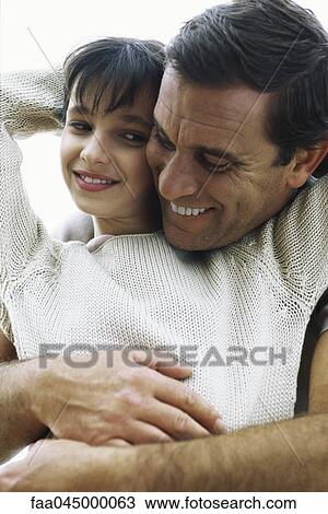 Stock Image - Father embracing daughter from behind, cheek to cheek, both smiling. Fotosearch