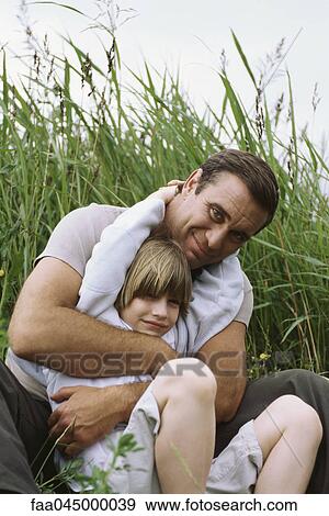 Father embracing son, sitting outdoors in tall grass View Large Photo Image Stock Photo - Father embracing son, sitting outdoors in tall grass. Fotosearch