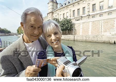 Stock Photograph - France, Paris, mature couple holding video camera and map, Seine River in background. Fotosearch